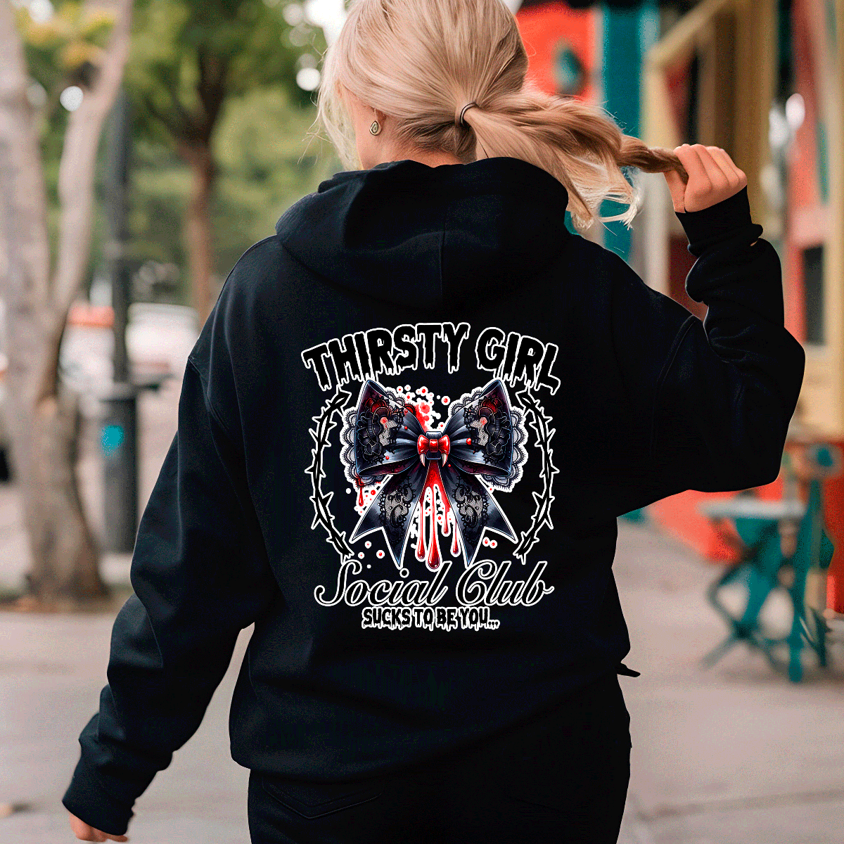 Person wearing a black hoodie with 'Thirsty Girl Social Club' design on the back, walking outdoors.