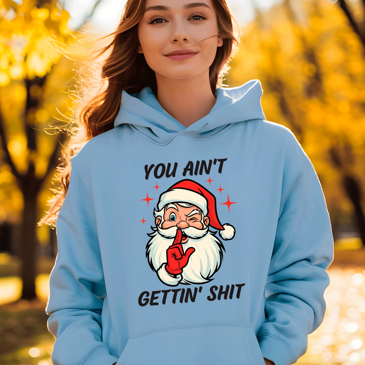 Person wearing a light blue hoodie with a graphic of Santa Claus and text, standing outdoors with trees in the background.