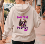 Person wearing a hoodie with festive design and text, holding a coffee cup.