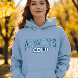 Person wearing a light blue hoodie with 'ALWAYS COLD' text in an outdoor setting with trees.