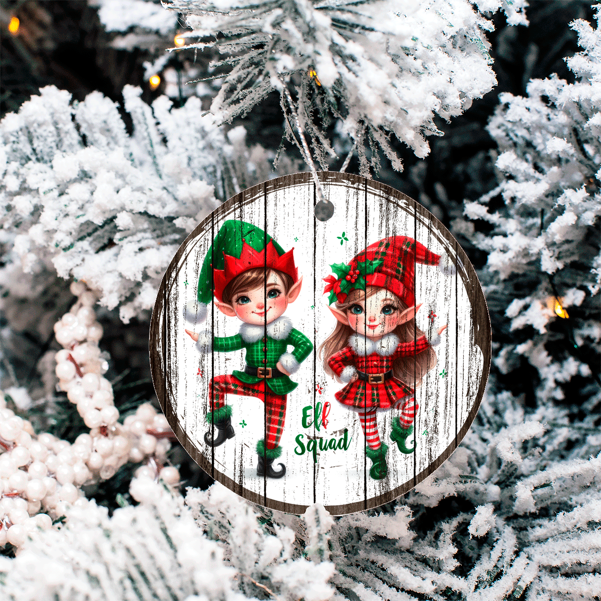 Circular Christmas ornament with two elves on a wooden background, hanging on a decorated tree.