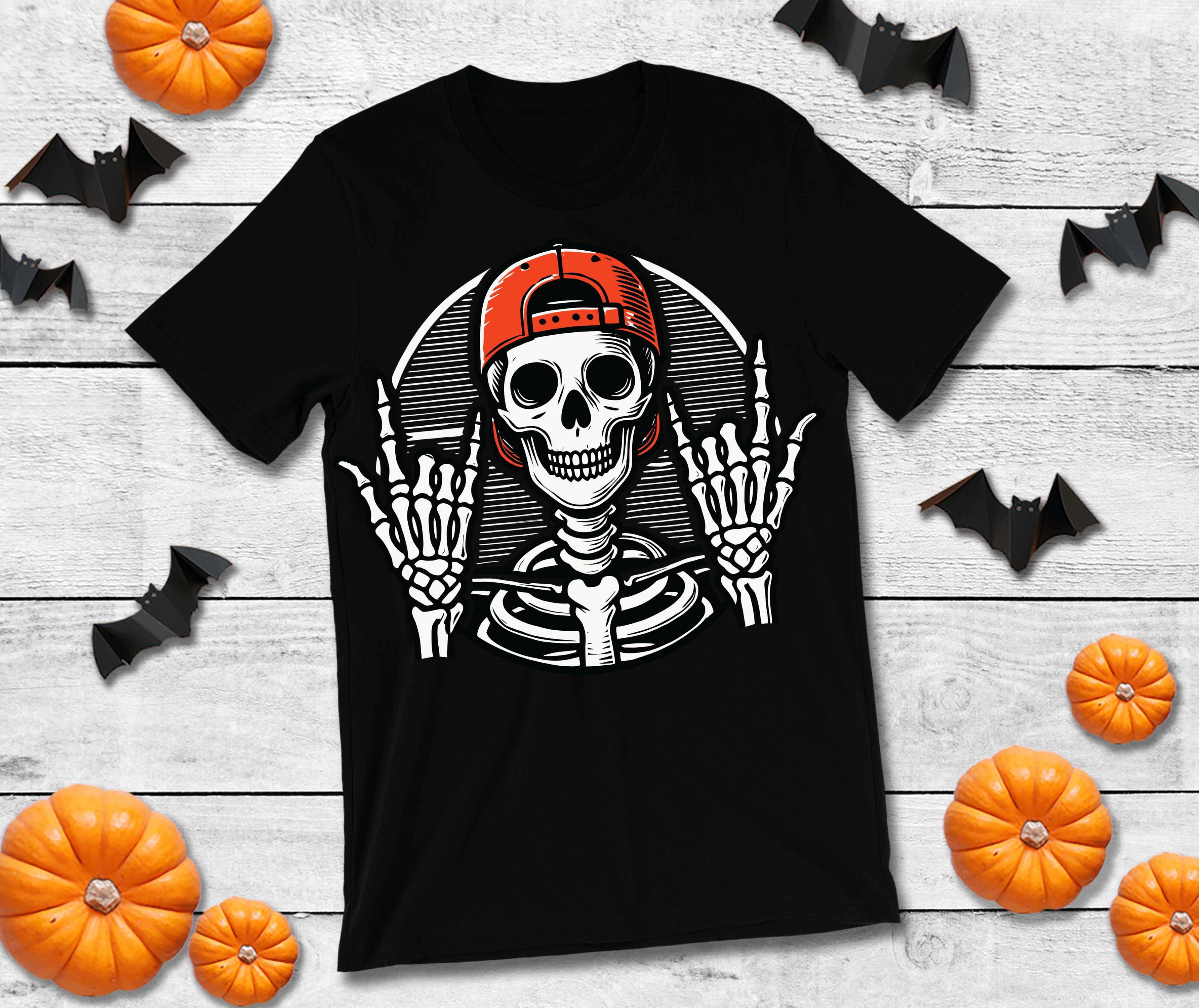 Black t-shirt with a skeleton wearing a red cap on a wooden surface with Halloween decorations.