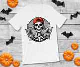 White t-shirt with a skeleton wearing a red cap design, surrounded by Halloween decorations on a wooden surface.
