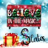 Christmas-themed sign with 'Believe in the Magic' text, presents, and snowflakes on a blue background.