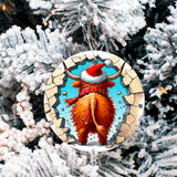 Round Christmas ornament with a bull wearing a Santa hat and scarf, hanging on a snowy tree.