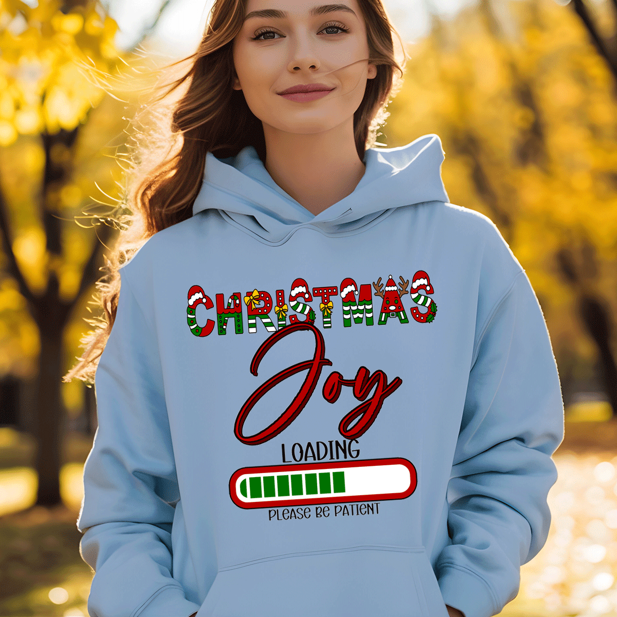 Person wearing a light blue hoodie with 'Christmas Joy Loading' text in an autumn setting
