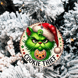 Christmas ornament with a green character wearing a Santa hat and 'Cookie Thief' text, hanging on a snow-covered tree.