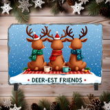 Three cartoon deer wearing Santa hats and scarves, sitting at a table with mugs and Christmas decorations on a wooden background.