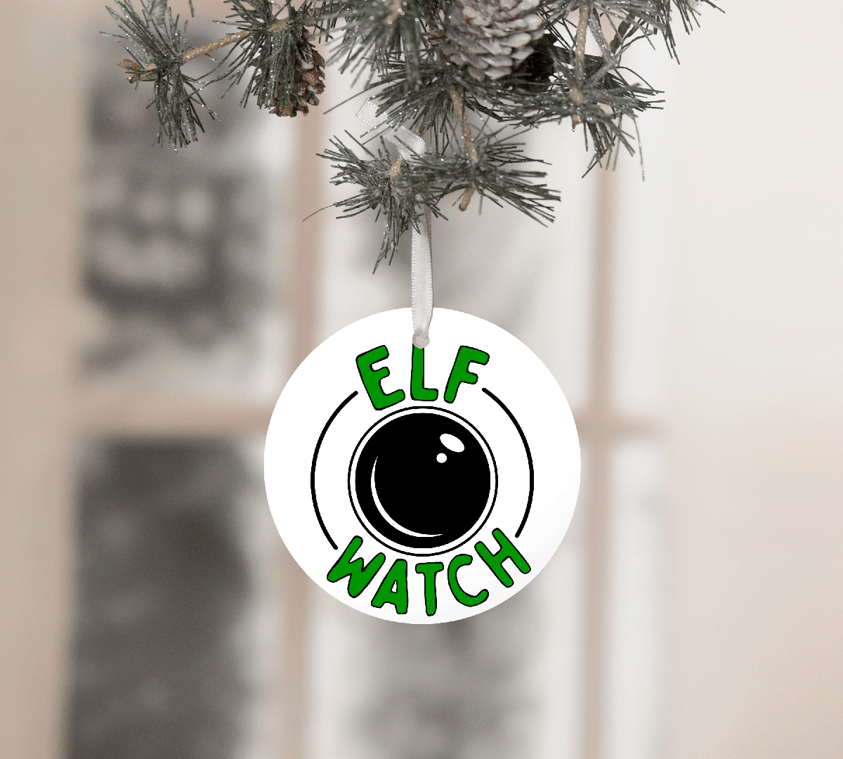 Ornament with 'Elf Watch' design hanging on a Christmas tree.