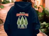 Navy blue hoodie with Christmas tree design and text on the back, worn by a person.