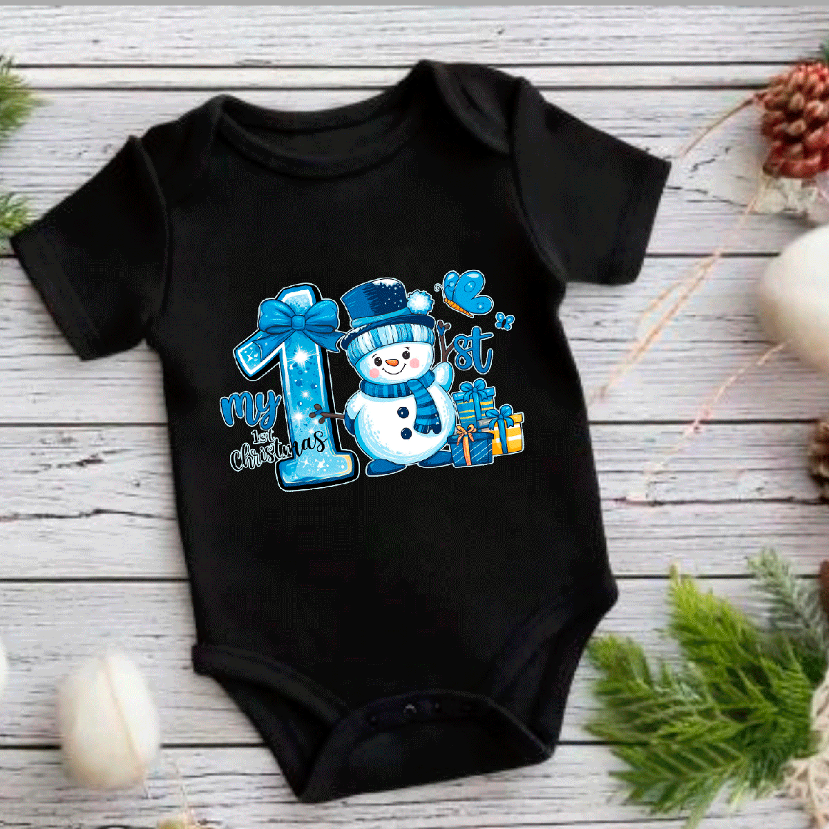 Black baby onesie with a snowman design and text on a wooden surface with Christmas decorations.