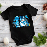 Black baby onesie with a snowman design and text on a wooden surface with Christmas decorations.