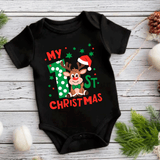Black baby onesie with Christmas-themed design featuring a reindeer and text on a wooden surface.