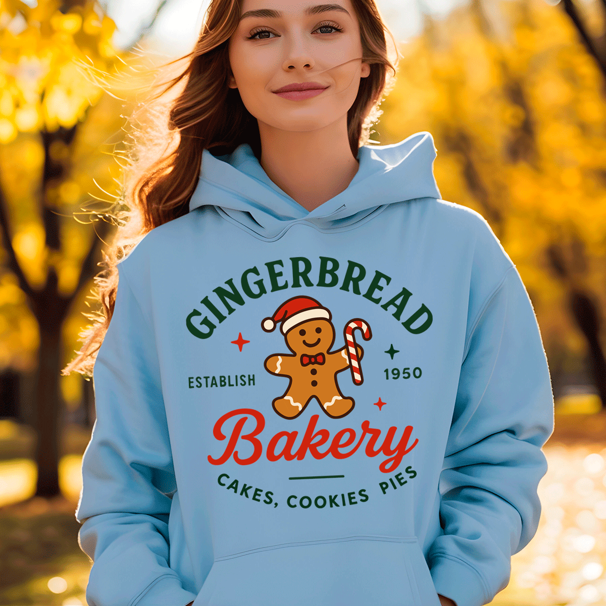 Person wearing a light blue hoodie with a gingerbread-themed design in an autumn setting.