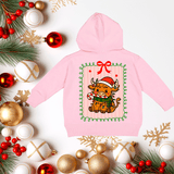 Pink hoodie with a Christmas cow design on a decorative background with ornaments and greenery.