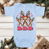 Light blue baby onesie with reindeer design and 'Ho Ho Ho' text on a wooden surface with Christmas decorations.