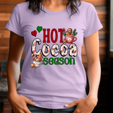 Person wearing a purple t-shirt with 'Hot Cocoa Season' text and graphics.