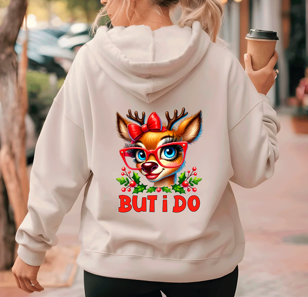 Person wearing a hoodie with a reindeer design and 'BUT I DO' text, holding a coffee cup.