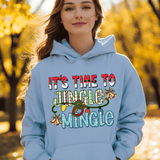 Person wearing a light blue hoodie with 'It's Time to Jingle & Mingle' text in an autumn setting