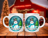 Two white mugs with a snowman design and 'Let it Snow!' text on a wooden surface.