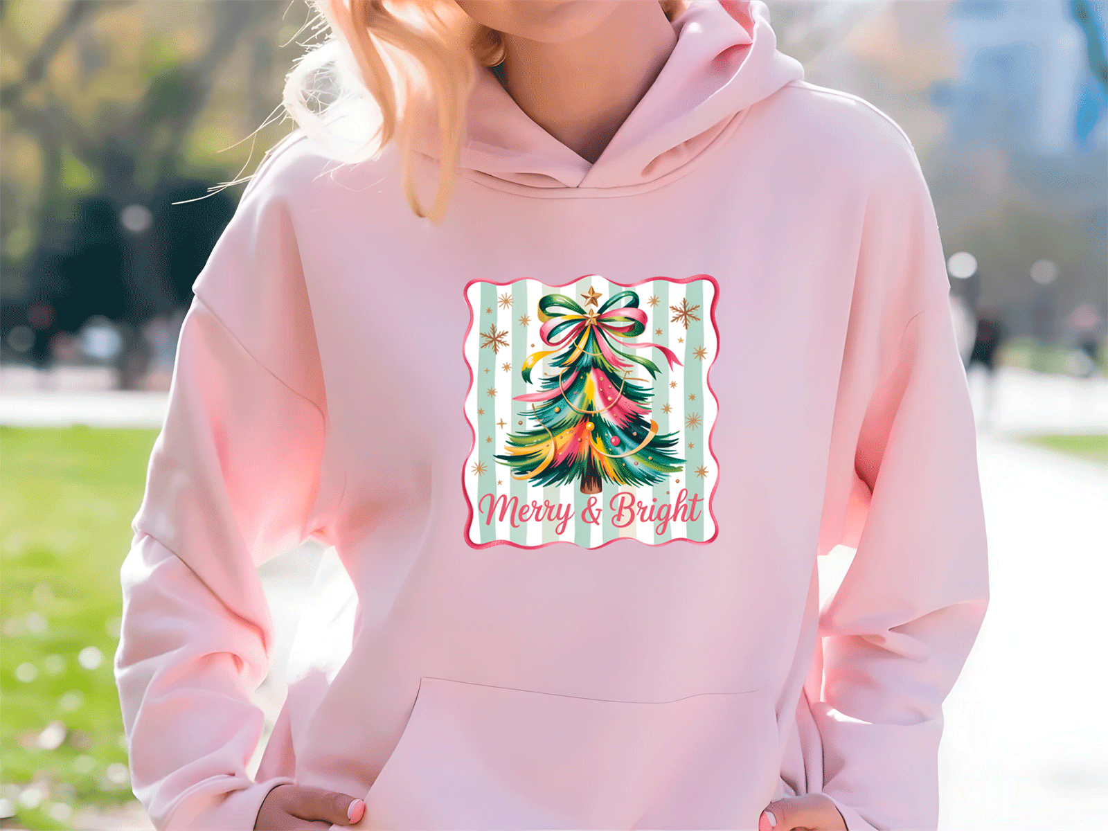 Person wearing a pink hoodie with a colorful Christmas tree design and 'Merry & Bright' text.