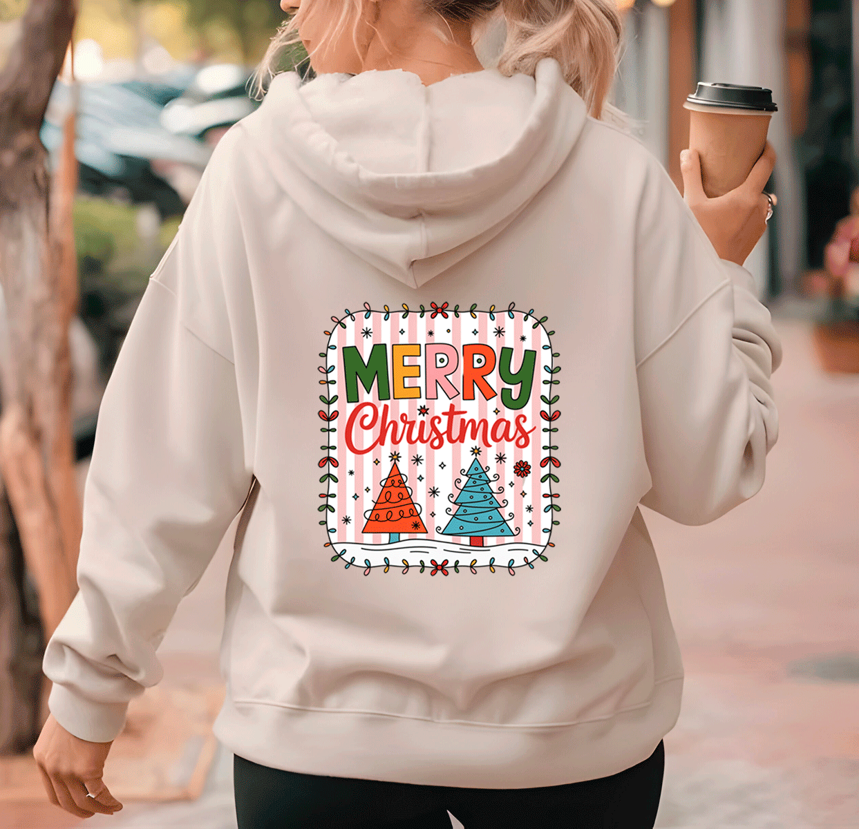 Person wearing a light gray hoodie with a 'Merry Christmas' design, holding a coffee cup.