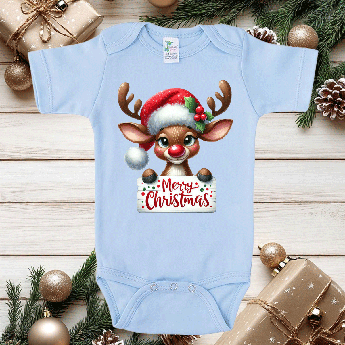 Light blue baby onesie with a Christmas reindeer design on a wooden surface with holiday decorations.
