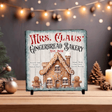 Decorative sign for 'Mrs. Claus' Gingerbread Bakery' with a gingerbread house design on a wooden surface.