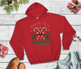 Red hoodie with 'North Pole University' design on a wooden surface with Christmas decorations.