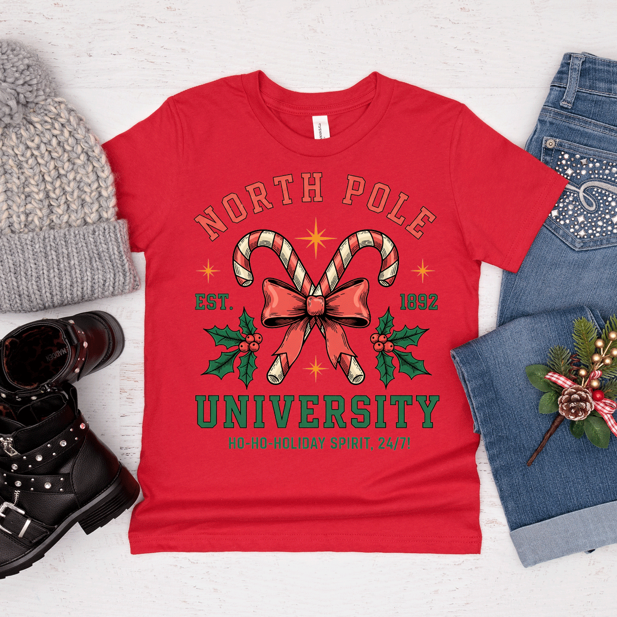 Red t-shirt with 'North Pole University' design, surrounded by festive items on a light background