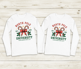 Two white long-sleeve shirts with 'North Pole University' design on a wooden surface