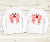 Two white long-sleeve shirts with pink bows and reindeer antlers on a wooden surface.