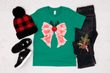 Green t-shirt with pink bow design, black jeans, red and black checkered beanie, and black shoes on a light gray background.