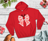 Red hoodie with a pink bow and reindeer design on a wooden surface with Christmas decorations.
