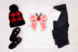 White shirt with pink bow design, red and black checkered hat, black shoes, and black jeans on a light wooden surface.