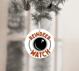 Round ornament with 'Reindeer Watch' text hanging on a Christmas tree.