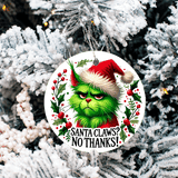 Christmas ornament with Grinch face and text 'Santa Claws? No Thanks!' on a snowy tree background
