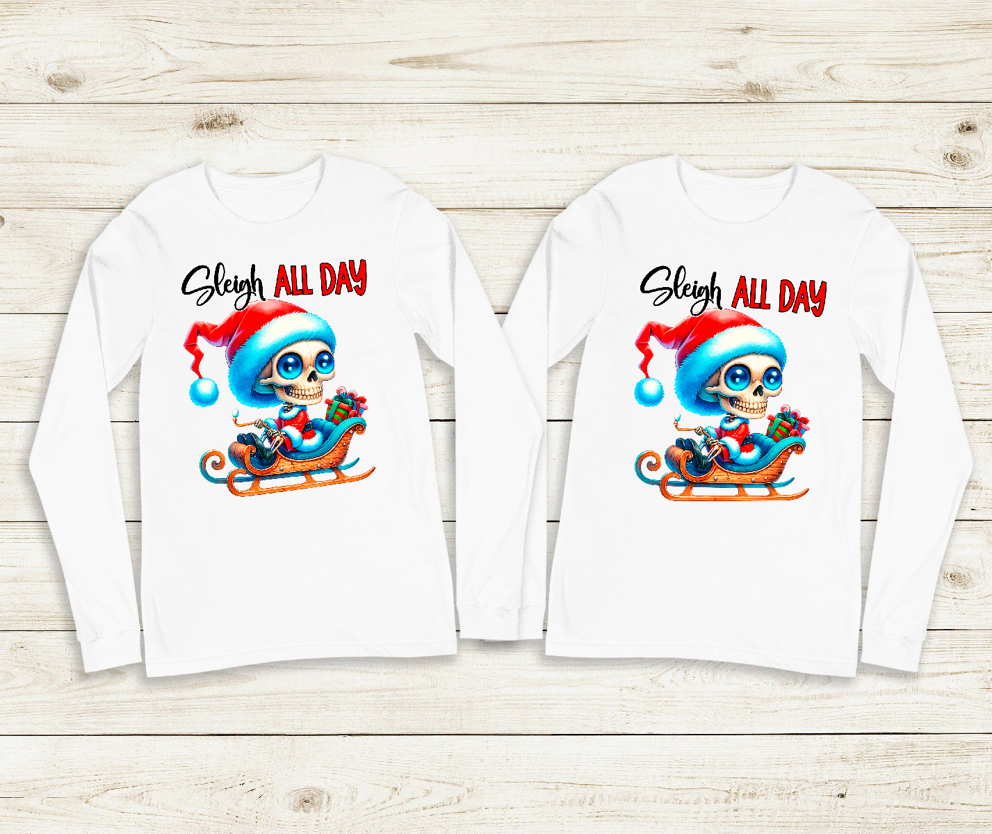Two long-sleeve shirts with a graphic of a skeleton in a Santa hat and sleigh, with 'Sleigh All Day' text, on a wooden surface.