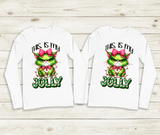 Two white long-sleeve shirts with a festive design featuring a green character with a pink bow and text on a wooden background.