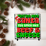 Christmas-themed slate with humorous text surrounded by pine cones and greenery on a white wooden background